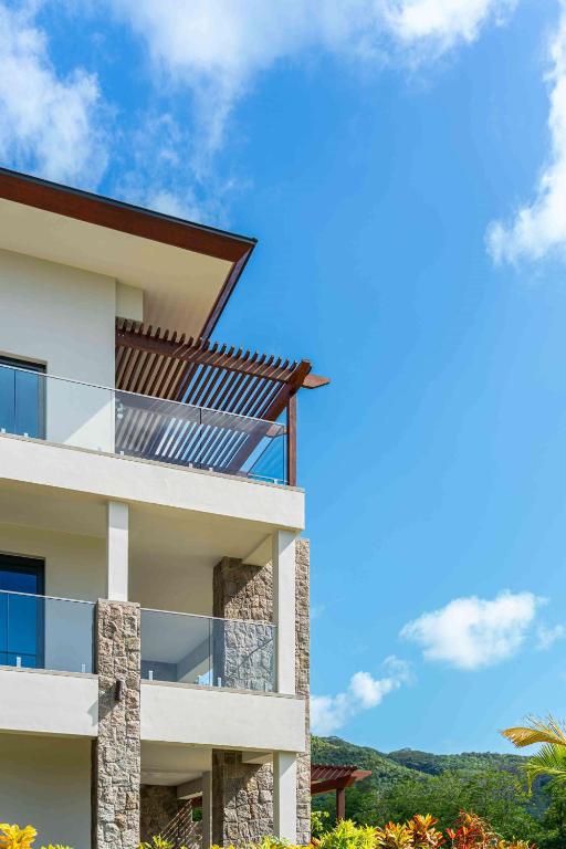 Modernas arhitektūras māja ar stikla balkonu un akmens elementiem, pret debesīm ar dažiem mākoņiem.