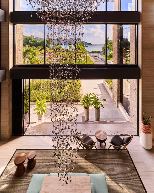 Mūsdienīgs viesnīcas interjers ar liela izmēra logiem, caur kuriem redzams skaists dārza skats un pludmale. Telpā ir eleganta gaismas ķermeņa instalācija un moderni mēbeļu elementi.