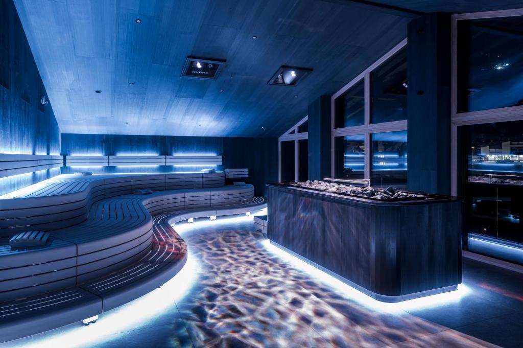 Mūsdienīga sauna ar zilu apgaismojumu un koka elementiem, kurā ir ērti sēžamie krēsli un plašas logu vitrīnas. Iekšējā telpa rada relaksējošu atmosfēru.