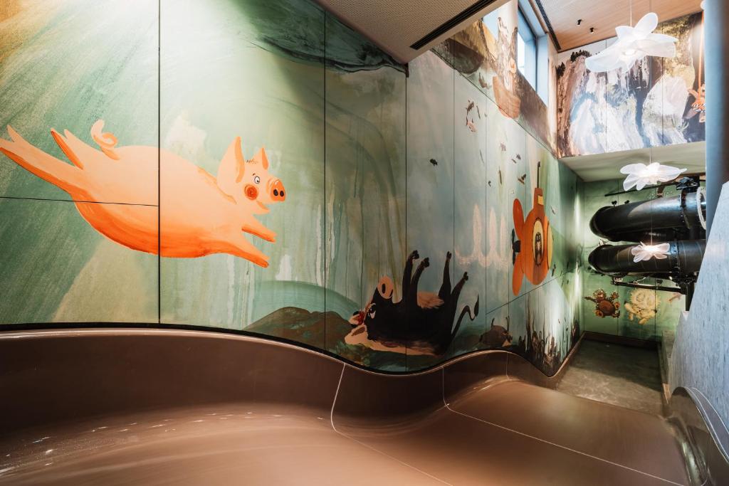 Krāsainas mākslas gleznas ar lidojošiem cūciņām un citiem dzīvniekiem, kas rotā slidkalniņu telpu. Šī vide ir dzīvīga un bērniem draudzīga, veidojot jautru atmosfēru.