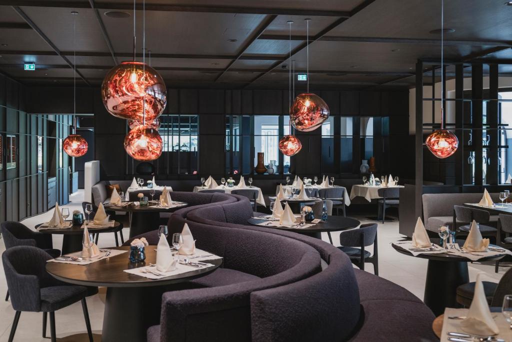 Mūsdienīgs restorāns ar elegantiem galdiem, dekorētiem ar salvetēm un grezniem apgaismojuma elementiem. Interjers ir melns ar siltām akcentiem, radot viesmīlīgu atmosfēru.