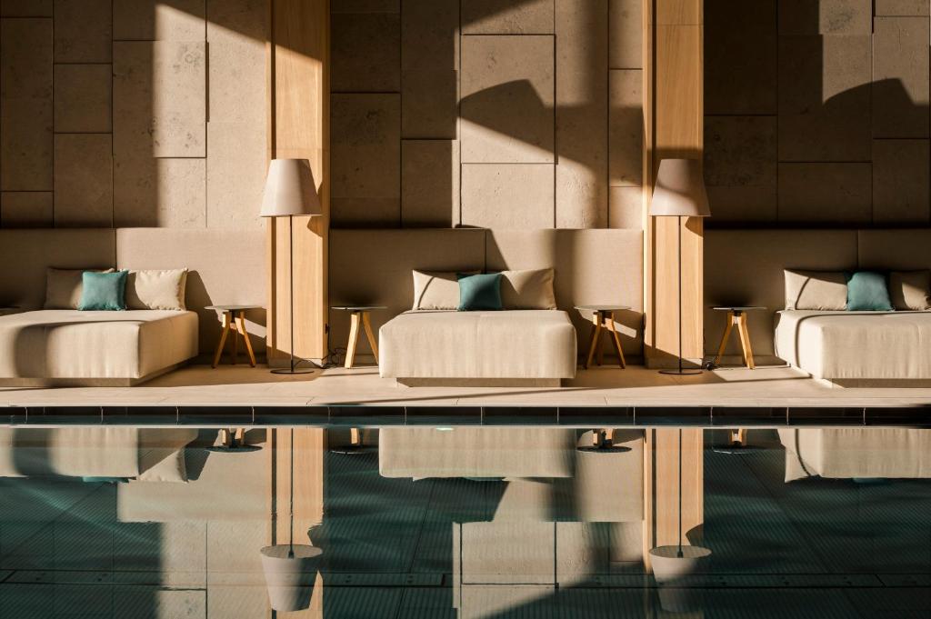 Mūsdienīgs spa telpa ar komfortablām atpūtas vietām, apgaismota ar dabiskiem saules stariem, un atspoguļojums baseinā.