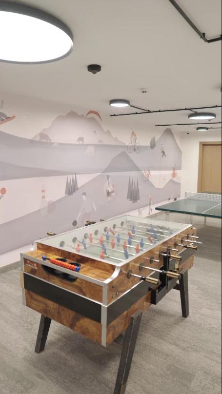 Galda futbols, kas novietots modernā telpā ar stilīgu sienas gleznojumu, kas attēlo dažādas sportiskas aktivitātes.