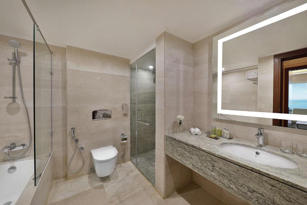 Mūsdienīgs vannas istabas interjers ar stikla dušu, akmens izlietni un elegantu spoguli. Telpai piemīt gaišas krāsas un tīra, minimālistiska estētika.