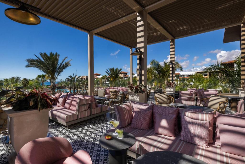 Elegants terases interjers ar rozā dīvāniem un palmām, kas radīja relaksējošu atmosfēru. Apskatāms baseins un debesu skats ar mākoņiem.