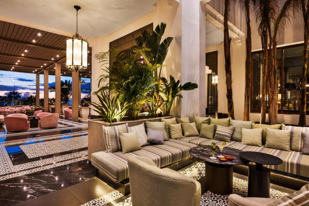 Mūsdienīgs viesnīcas vestibils ar greznu sēdvietu zonu, dekorēts ar zaļām augu kompozīcijām un elegantu apgaismojumu. Gaisotne ir relaksējoša, ideāla atpūtai un socializēšanai.