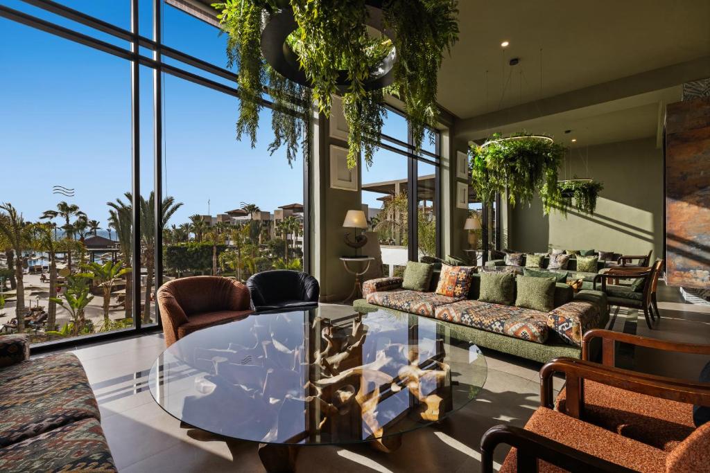 Lieliska un moderna viesnīcas atpūtas zona ar lieliem logiem, caur kuriem redzama ainava ar palmām un baseinu. Interjerā ir zaļi augi un komfortabli dīvāni, radot relaksējošu atmosfēru.