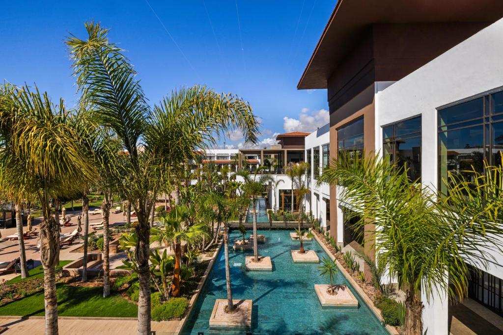 Moderns kūrorts ar palmām un ūdens elementiem, kas piešķir relaksējošu atmosfēru. Šis attēls atspoguļo elegantu ainavu ar skaidru zilo debesu fonu.