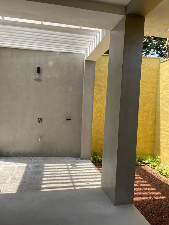 Mūsdienīga, gaiša āra duša ar betona sienām un spilgti dzeltenu fona sienu, kas rada relaksējošu atmosfēru. Saules stari iekrīt caur jumta slēģiem, piešķirot telpai unikālu apgaismojumu.