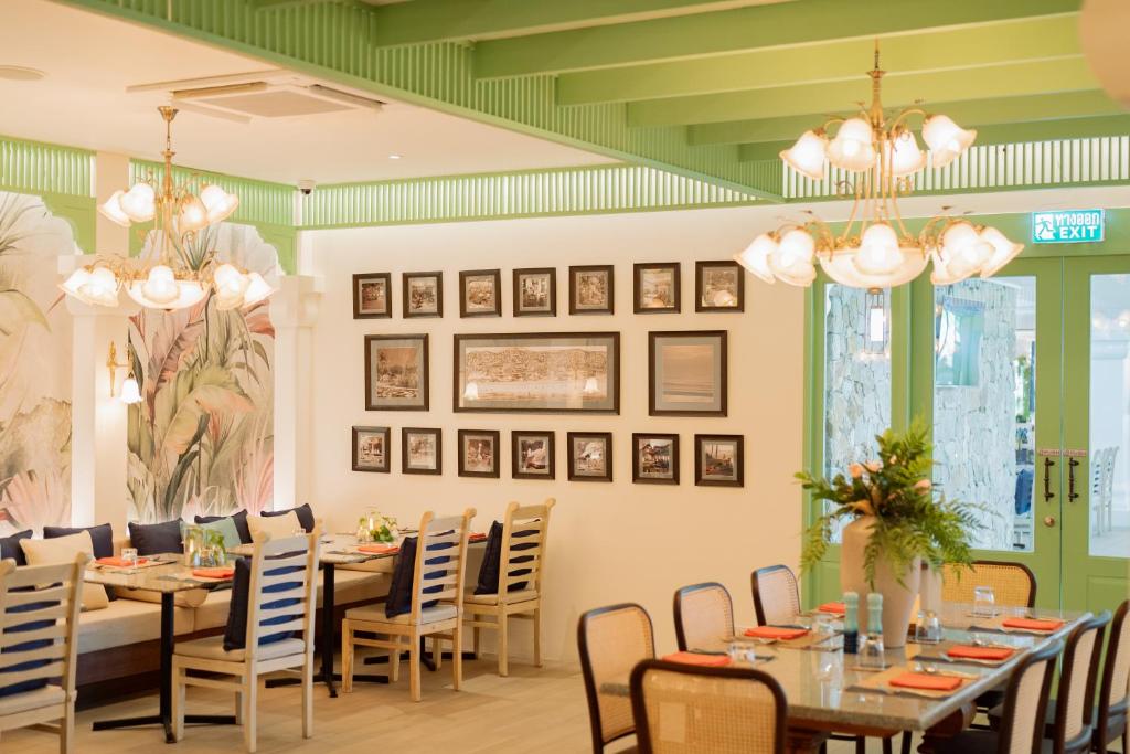 Gaišs un moderns restorāns ar zaļu interjeru, dekoratīviem gleznojumiem un elegantiem gaismas ķermeņiem. Pie galda redzami galda piederumi un ziedu kompozīcija.