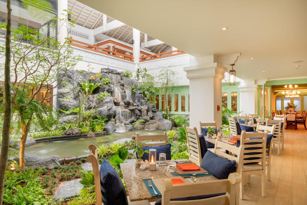 Restorāna interjers ar gleznainu ūdenskritumu un zaļo veģetāciju, radot mierīgu atmosfēru. Galdi ir sakārtoti ar dekoratīvām detaļām un ziediem.