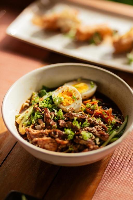 Svaiga un garšīga nūdeles bļoda ar ceptu gaļu, dārzeņiem un vārītu olu, rotāta ar zaļajiem sīpoliem un sezama sēklām.