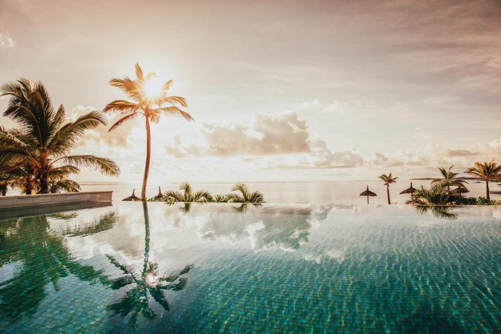 Eleganta baseina ainava ar palmu kokiem un saulrietu, atspoguļojoša ūdenī. Ideāla tropu atpūtas atmosfēra.