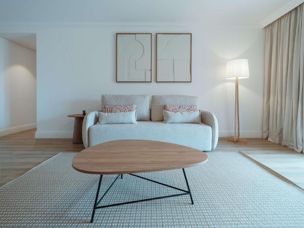 Mūsdienīgs viesistabas interjers ar gaišām krāsām, dīvānu un stilīgu galdu, radot komfortablu un elegantu atmosfēru.