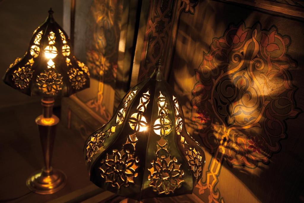 Eleganti lampas ar izsmalcinātu rakstu, kas izstaro siltu gaismu un rada mājīgu atmosfēru. Fons ar krāsainu ornamentu papildina interjera dizainu.