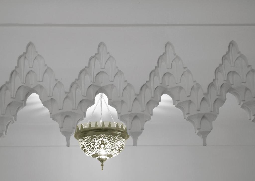 Balta interjera dizains ar arābu stilā veidotu lustras gaismu un dekoratīvām arhitektūras detaļām.
