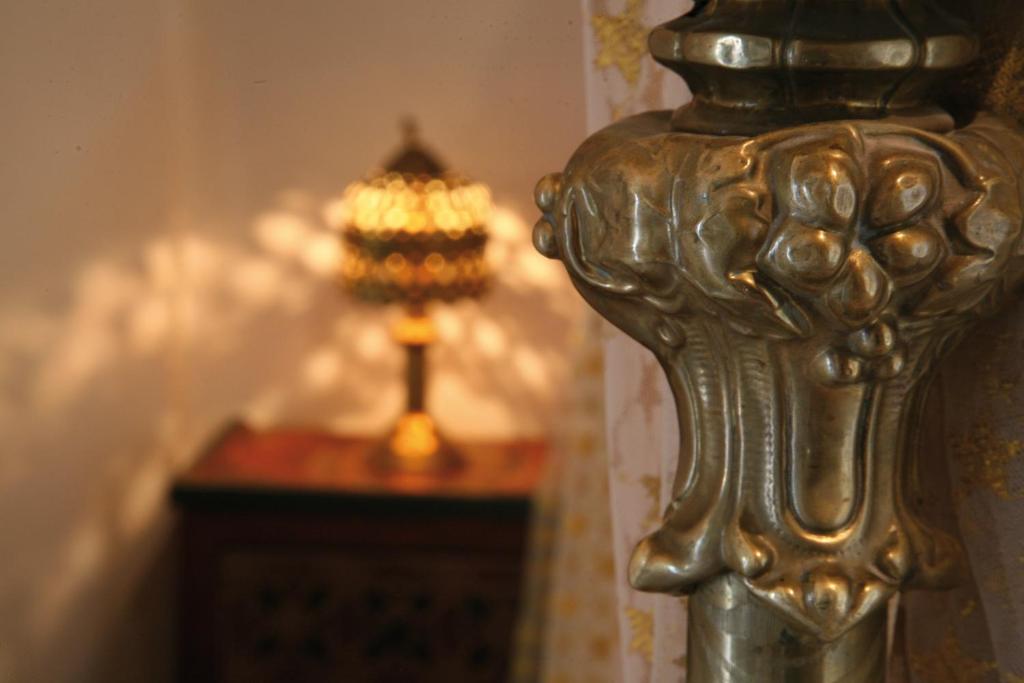 Antīks lampas statīvs ar izsmalcinātu dizainu un zeltītu lampu, kas izgaismo telpu. Gaismas atspīdējumi rada siltu atmosfēru.