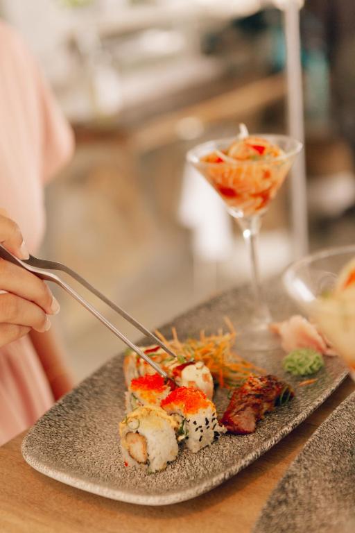 Svaigas sushi šķēles uz greznas keramikas trauka, kam blakus stāv kokteilis ar garnelēm.