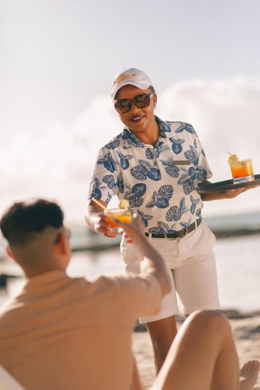 Pludmales apkalpotāja pasniedz dzērienus apmeklētājam, baudot saulainu dienu. Apskatāms atpūtas brīdis pie jūras ar kokteiļiem.