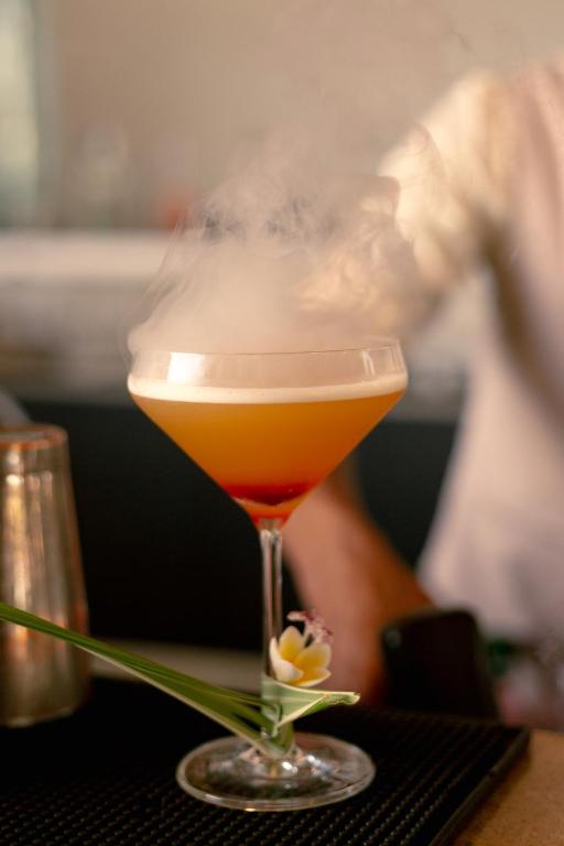 Kokteilis ar tvaiku, pasniegts eleganta glāzē ar zieda dekoru un sarkanu kārtu apakšā.