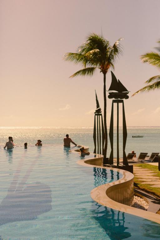 Peldbaseins ar skatu uz jūru, palmas un cilvēki, kas atpūšas saulainā pludmalē. Ideāla atmosfēra relaksācijai un atpūtai.