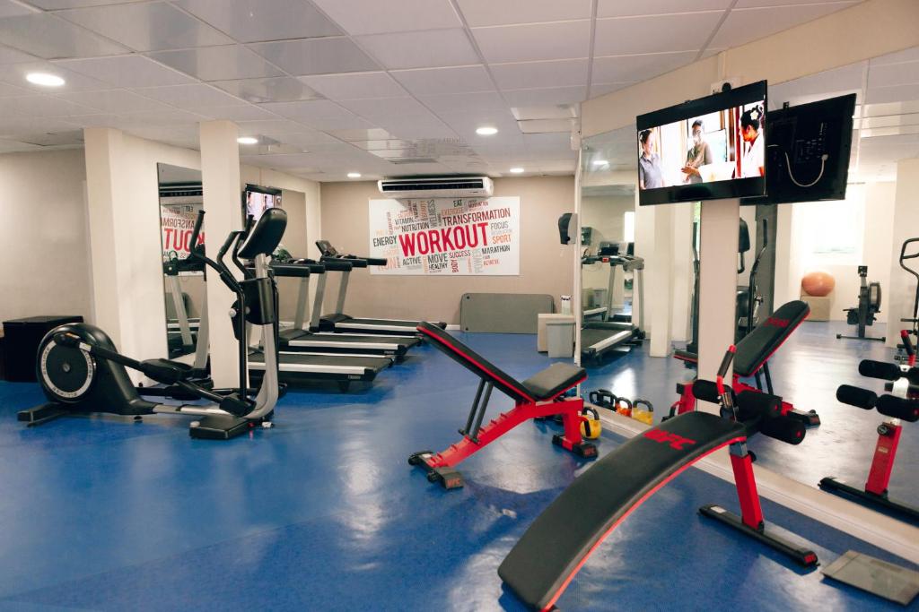 Mūsdienīga trenažieru zāle ar dažādiem trenažieriem un ekrānu, kas rāda vingrošanas programmas. Telpā ir gaiša apgaismojuma un sporta aprīkojuma kombinācija.