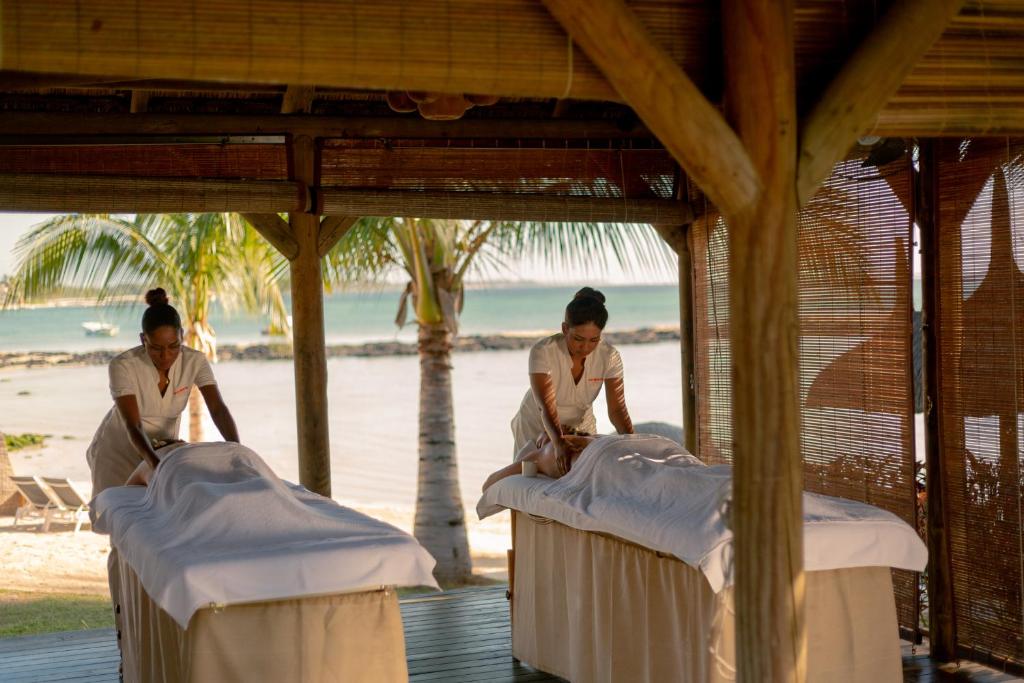 Divas masāžas speciālistes veic relaksējošas masāžas pludmales piekraste, izbaudot dabu un mierīgu atmosfēru.