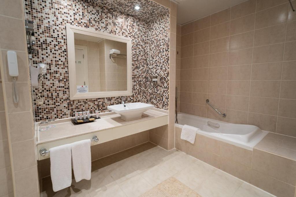 Mūsdienīga vannas istaba ar mozaīkas sienu, elegantu izlietni un vannu, kas piedāvā komfortu un stilu. Ideāla izvēle relaksācijai un atpūtai.