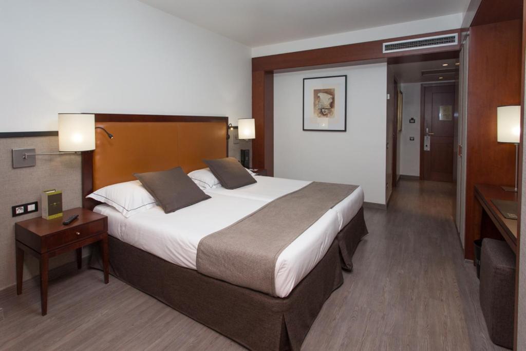 Mūsdienīgs viesnīcas numurs ar divām gultām, koka mēbelēm un siltām krāsām, radot patīkamu atmosfēru. Numurā ir eleganta apgaismojuma sistēma un piekļuve vannas istabai.