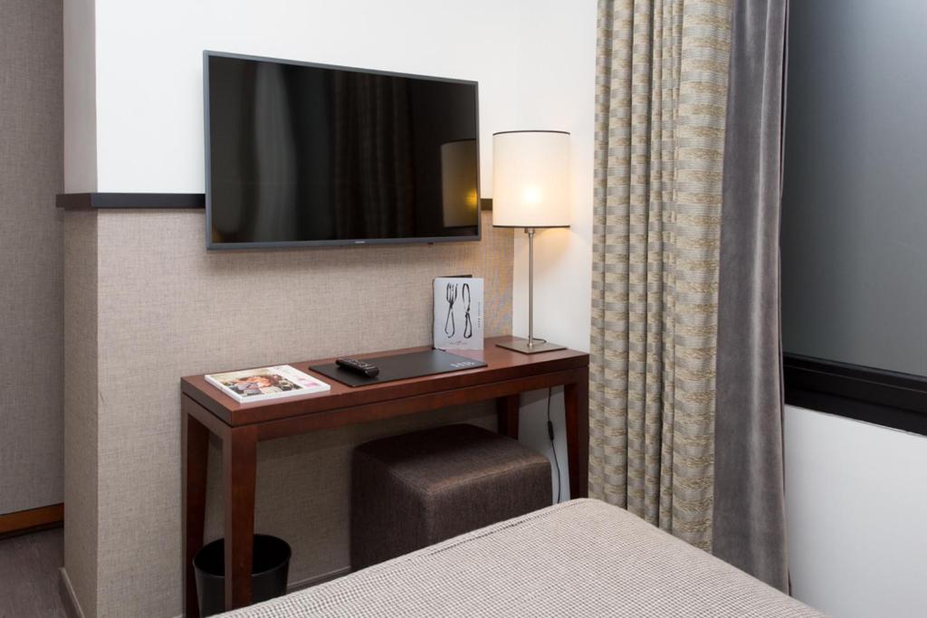 Mūsdienīga viesnīcas numura interjers ar plakanā ekrāna televizoru, galdu un lampu. Gaismas un tekstūras kombinācija rada patīkamu atmosfēru.