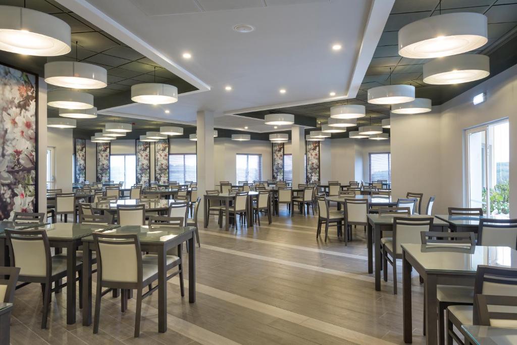 Mūsdienīgs restorāna interjers ar elegantiem galdiem un krēsliem, apgaismojums no piekārtajām lampām un ziedu sienu dekoriem. Ideāla vieta relaksējošai ēdienreizei.