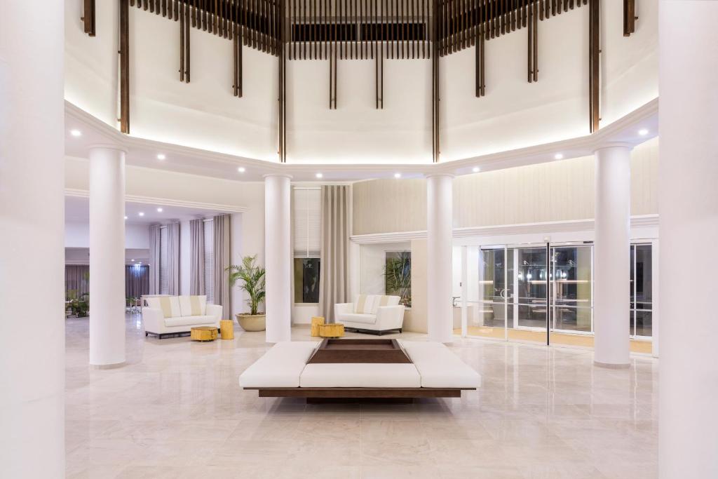 Mūsdienīgs viesnīcas vestibils ar elegantu baltu interjeru, plašām telpām un dabīgām augu dekorācijām. Gaisma un arhitektūra rada patīkamu un relaksējošu atmosfēru.