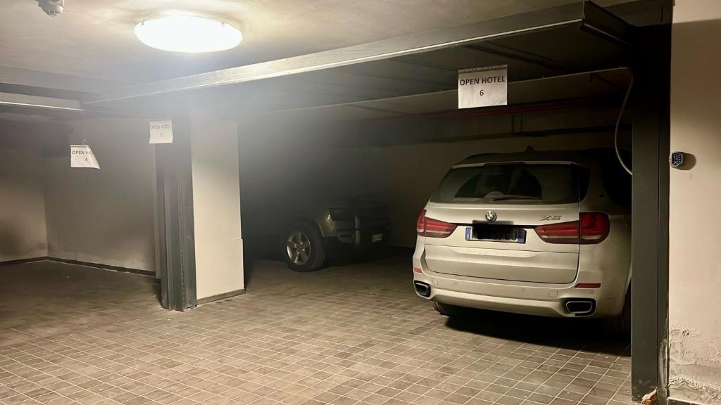 Garažas ar divām automašīnām un zīmēm "OPEN HOTEL"