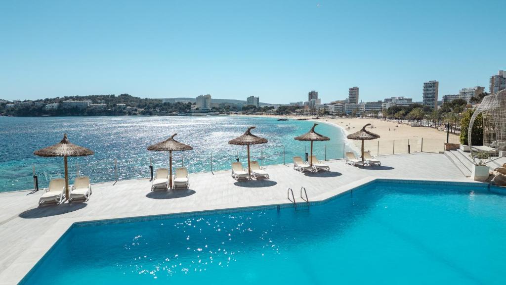 Peldbaseins ar sauļošanās krēsliem un saulessargiem, kas atrodas pie pludmales ar skatu uz jūru un pilsētas ainavu. Ideāla vieta atpūtai un relaksācijai.