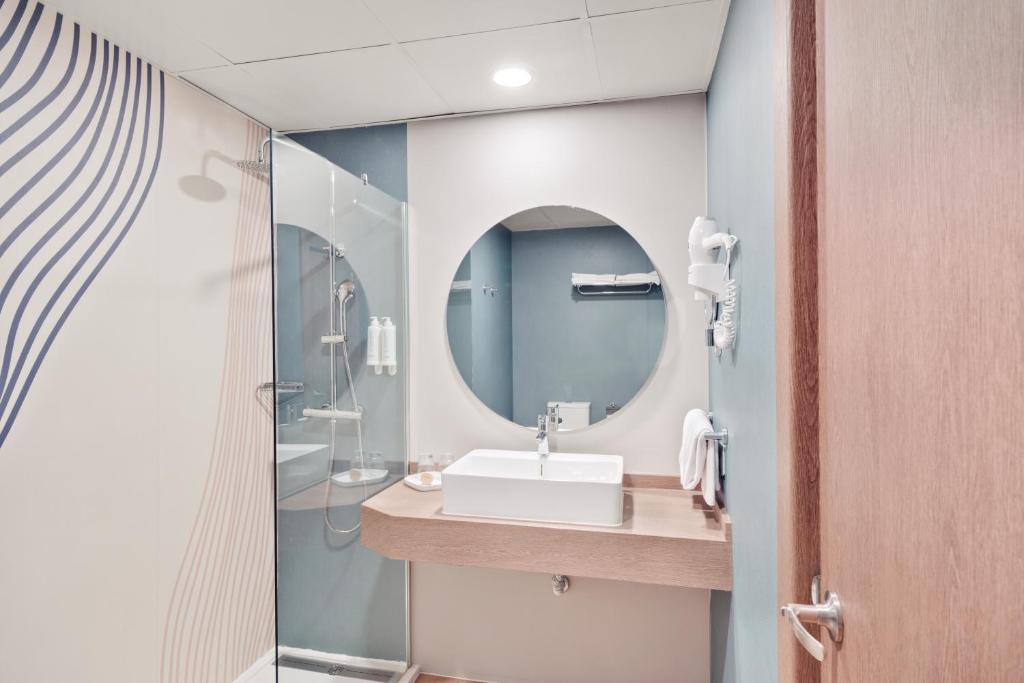 Mūsdienīgs vannas istabas interjers ar stikla dušu, apaļu spoguli un koka izskatu. Sienās ir stilizēti zīmējumi, kas piešķir telpai eleganci.