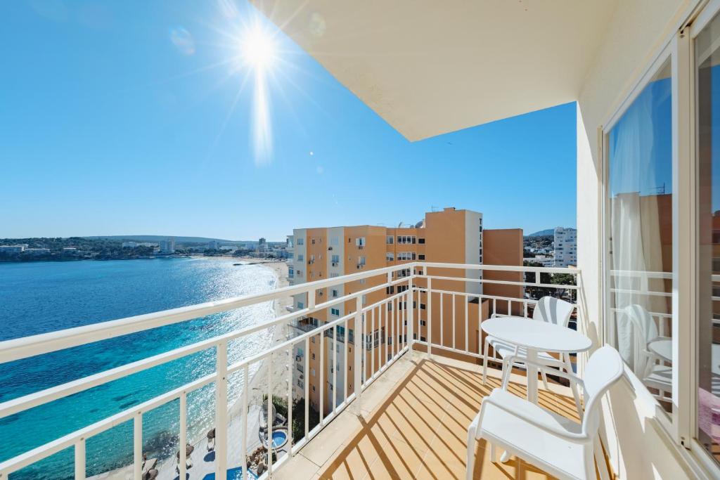 Saulaina terase ar skatu uz jūru, kurā redzama zila ūdens virsma un apkaime, ar divām baltām krēsliem un galdu. Ideāla vieta relaksācijai brīvā dabā.