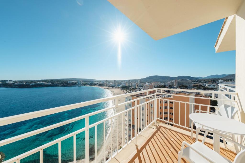 Skats no balkona uz jūru un pludmali, apgaismots ar spilgtu sauli, ar miera un atpūtas atmosfēru.