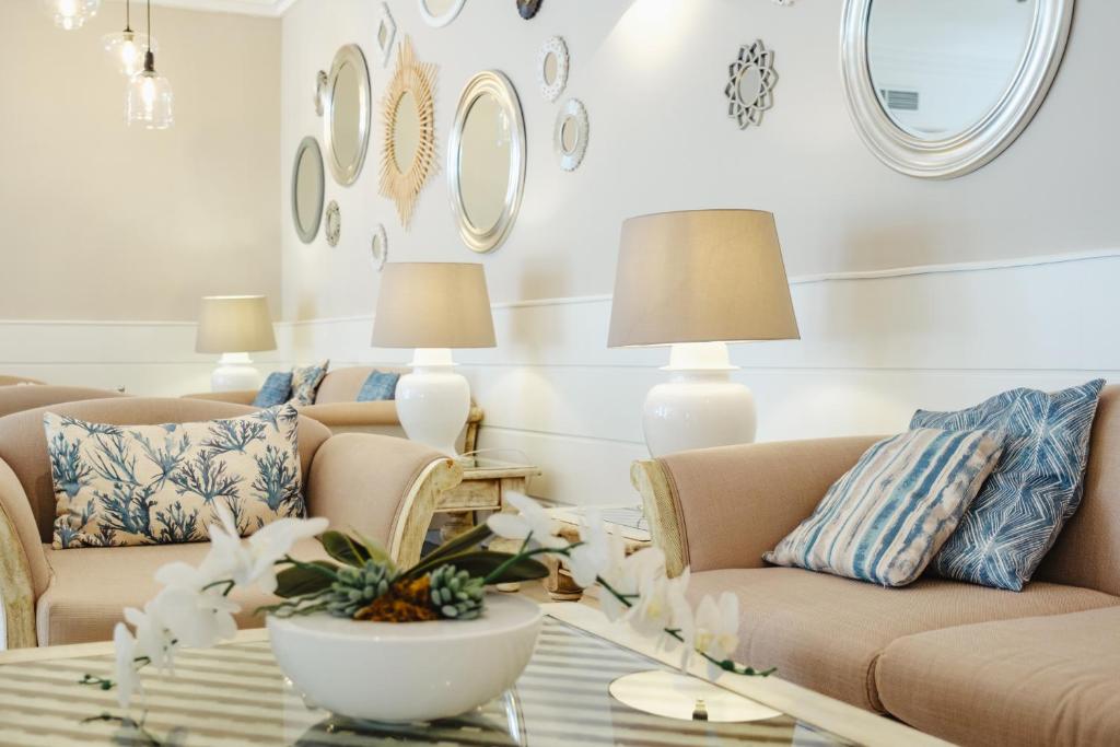 Mūsdienīgs viesistabas interjers ar elegantiem dīvāniem, dekoratīviem spilveniem un spoguļiem uz sienas. Gaismas elementi un ziedu kompozīcija piešķir telpai siltumu un mājīgumu.