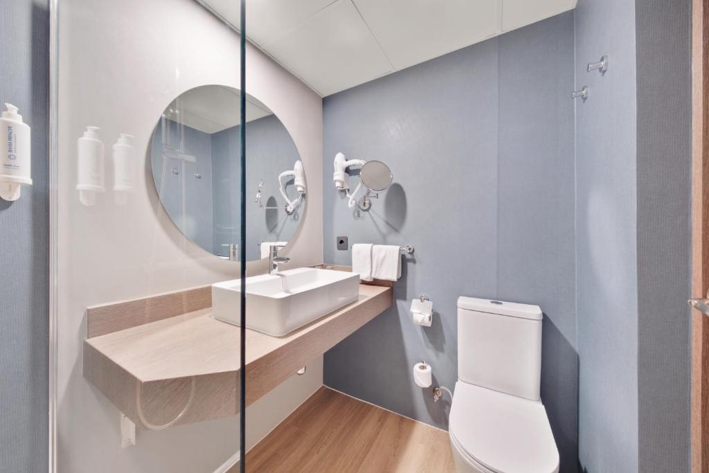 Mūsdienīgs un stilīgs vannas istabas interjers ar gaišām krāsām, apaļu spoguli un minimālistisku dizainu. Vannas istabā ir moderna izlietne un higiēnas piederumi.