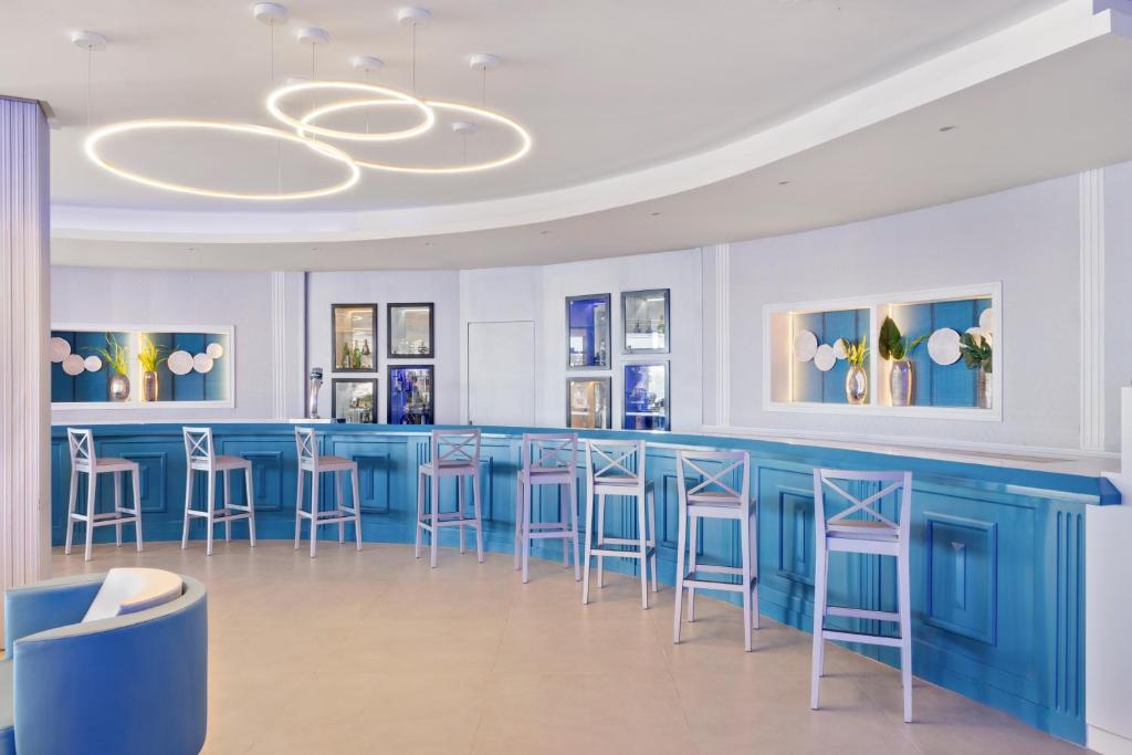 Moderns bārs ar zilām sienām un elegantiem gaismas elementiem, kas rada relaksējošu atmosfēru. Viegli koka krēsli un dekoratīvi elementi piešķir telpai stilīgu izskatu.