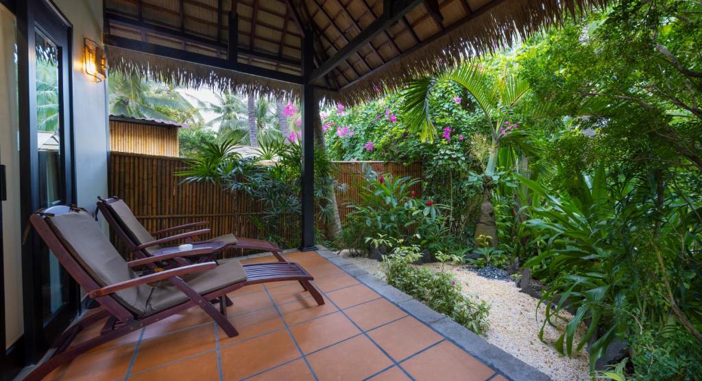 Mierīga terase ar divām atpūtas krēslām, ieskauta zaļumiem un ziediem, radot relaksējošu atmosfēru. Ideāla vieta atpūtai un meditācijai.