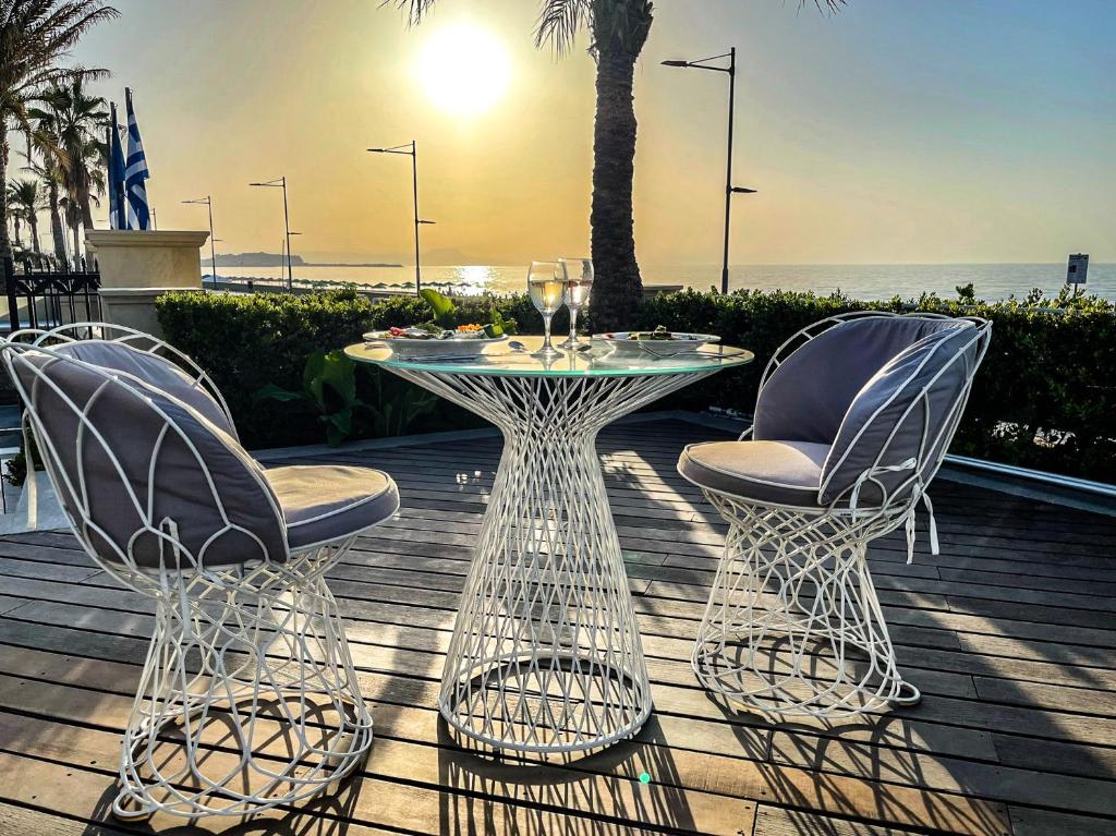 Romantisks skats uz jūru ar baltām vītņu krēsliem un stikla galdu, kas novietots terasē saulrieta gaismā. Ideāla vieta relaksācijai un baudīšanai.
