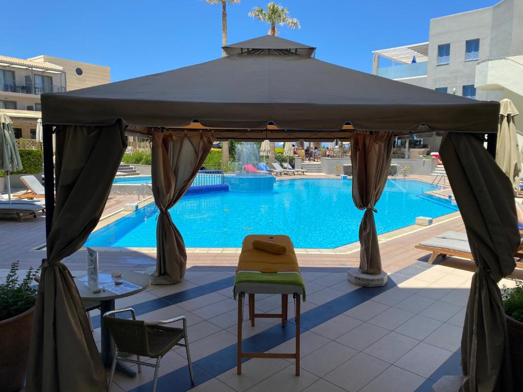 Peldbaseinsā esoša atpūtas zona ar gultām un saulessargiem, skatoties caur teltīm uz sauli apgaismoto baseinu. Ideāla vieta relaksācijai un atpūtai.