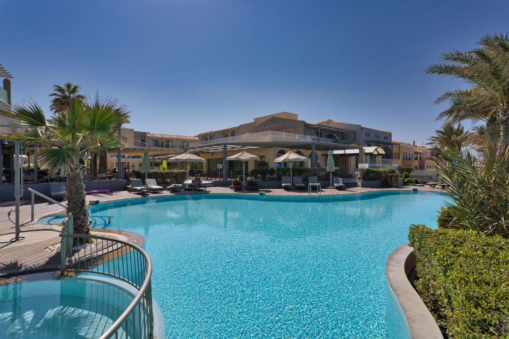 Luksusīgs baseins ar palmām un saulessargiem, kas atrodas viesnīcas pagalmā saulainā dienā. Ideāla vieta atpūtai un relaksācijai.