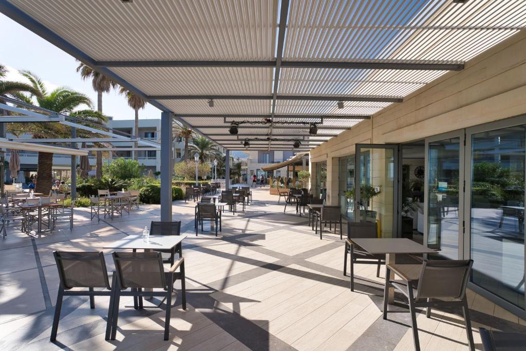 Moderns āra kafejnīcas terases skats ar galds un krēsli, apzaļumojums un palmām, saulains laiks.