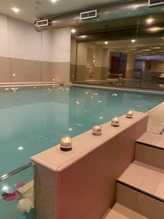 Mūsdienīgs peldbaseins ar zilu ūdeni, apgaismots ar svecēm un dekorēts ar ziedlapiņām. Interjers ir elegants un relaksējošs.