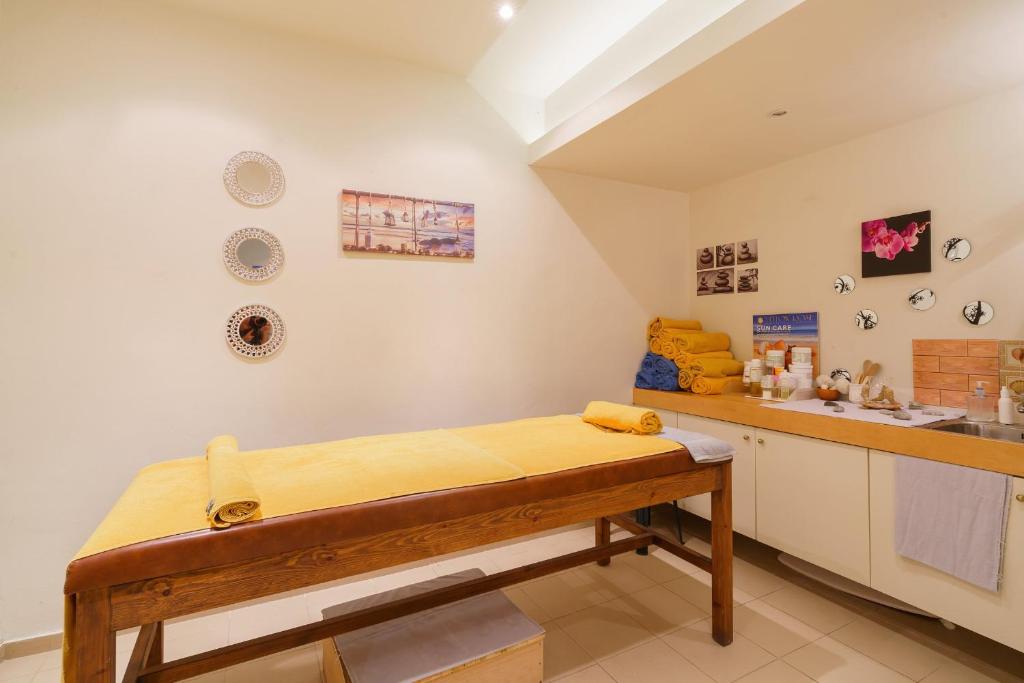 Skaista un mierīga masāžas telpa ar koka galdu, dzelteniem dvieļiem un dekoratīviem elementiem uz sienām. Telpā ir arī kosmētikas produkti un plaukti ar dvieļiem.