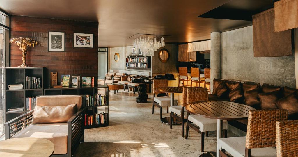 Mūsdienīgs kafejnīca ar elegantu interjeru, kurā ir brūni dīvāni, koka galdi un grāmatu plaukti. Telpa ir gaiša, ar lieliem logiem un stilīgiem dekoratīviem elementiem.