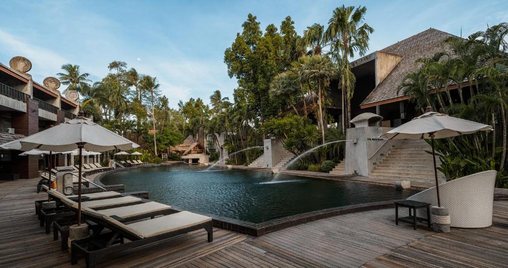 Elegants kūrorta baseins ar saulessargiem un kokiem apkārt, radot mierīgu atmosfēru. Ideāla vieta relaksācijai un atpūtai.