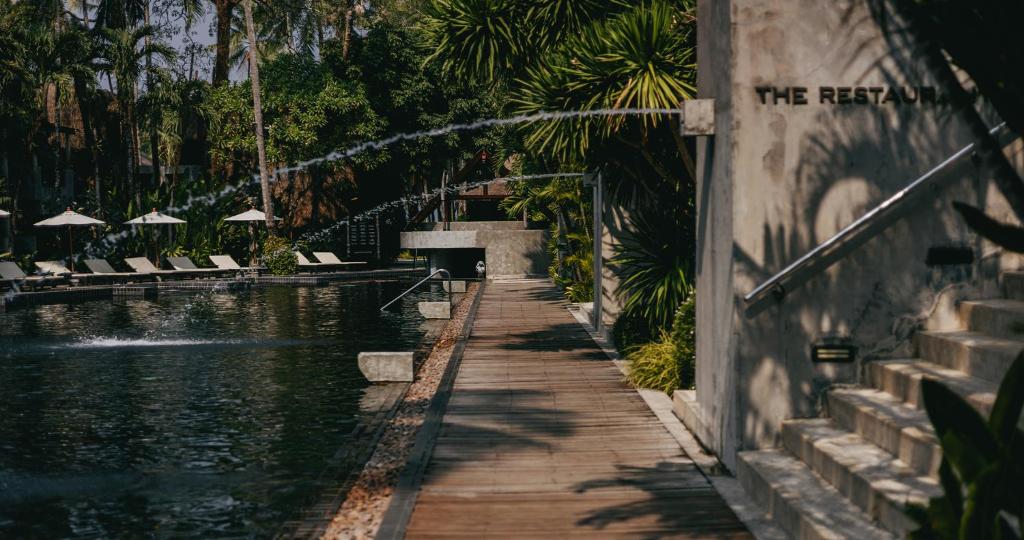 Atpūtas zona ar peldbaseinu un koka celiņu, kas ved uz restorānu, ieskauta zaļumiem un saules laukumiem. Ideāla vide relaksācijai un baudīšanai.